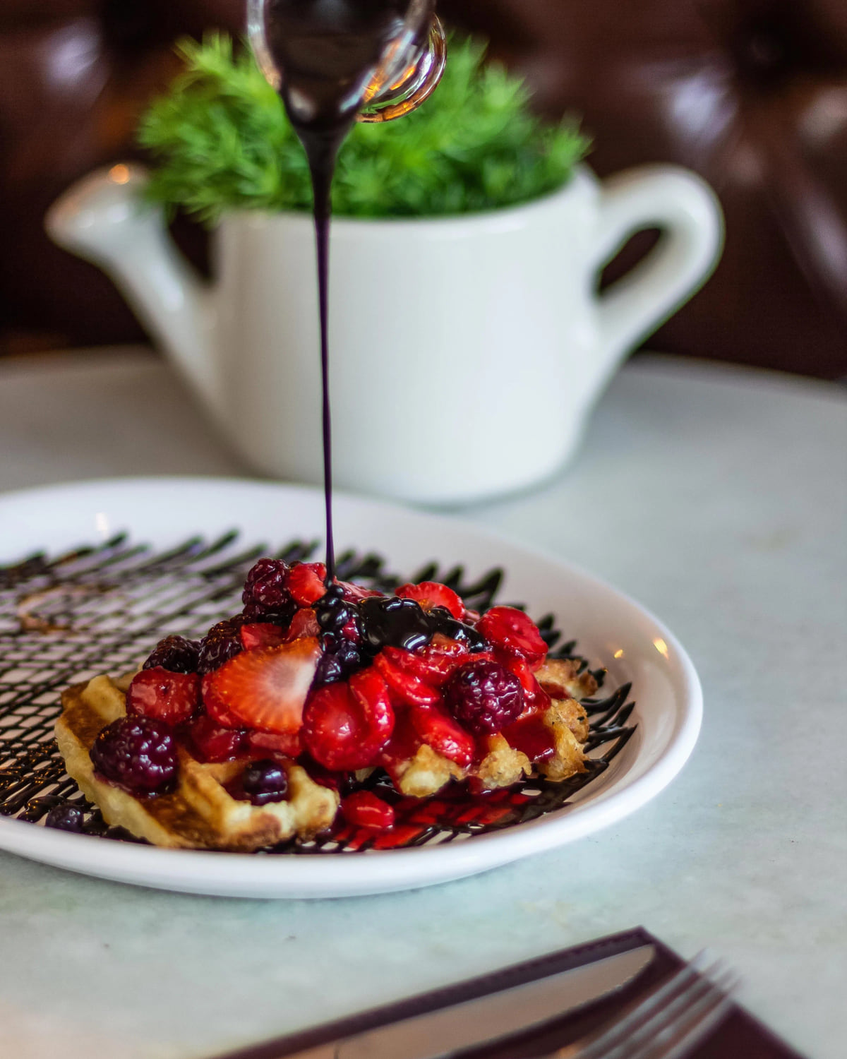 Waffle com frutas vermelhas e calda escorrendo sobre mesa de mármore do La Fleur Bistrô